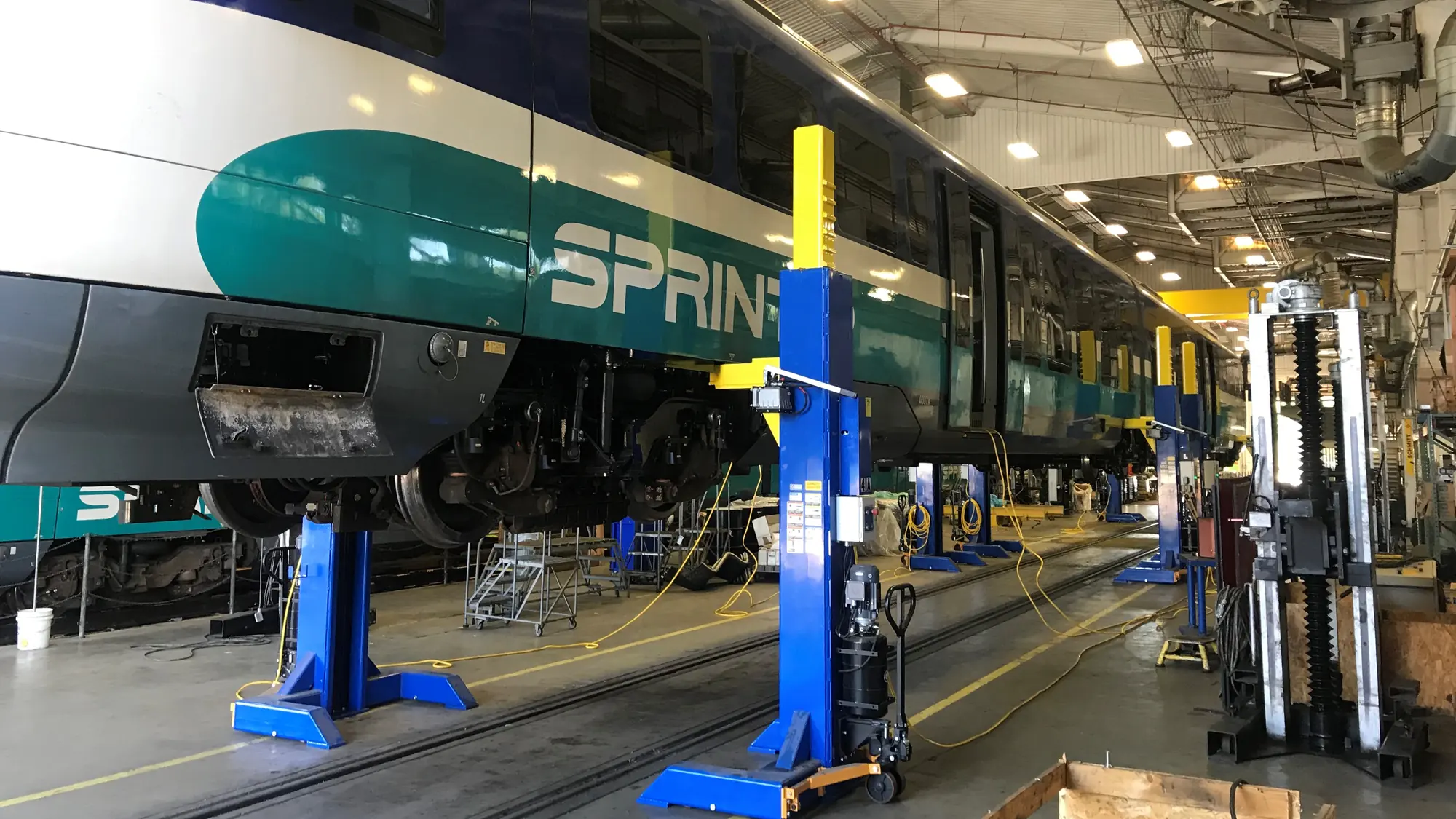 A SPRINTER light rail car raised on blue inground lifts inside a rail maintenance facility